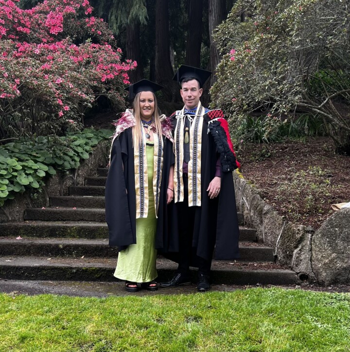 Dana pictured left, Levi pictured right in their graduation gowns in front of a garden